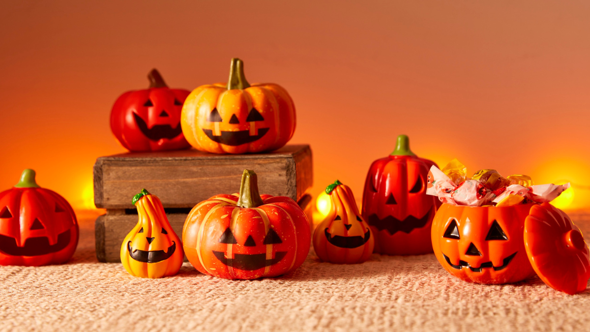 Colorful Halloween pumpkin decorations with smiling jack-o’-lantern faces, candy-filled pumpkin bucket, and warm glowing background.