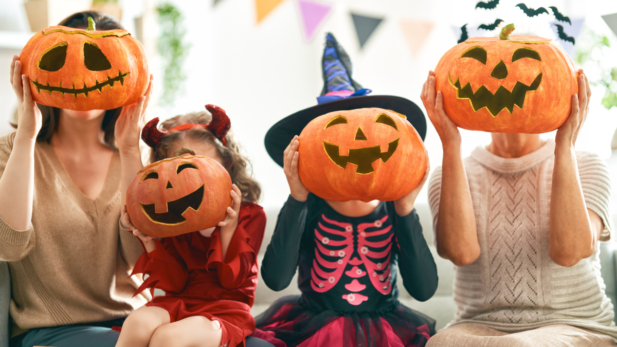 A family in fun Halloween costumes holding carved pumpkins with glowing jack-o’-lantern faces, celebrating spooky season together.