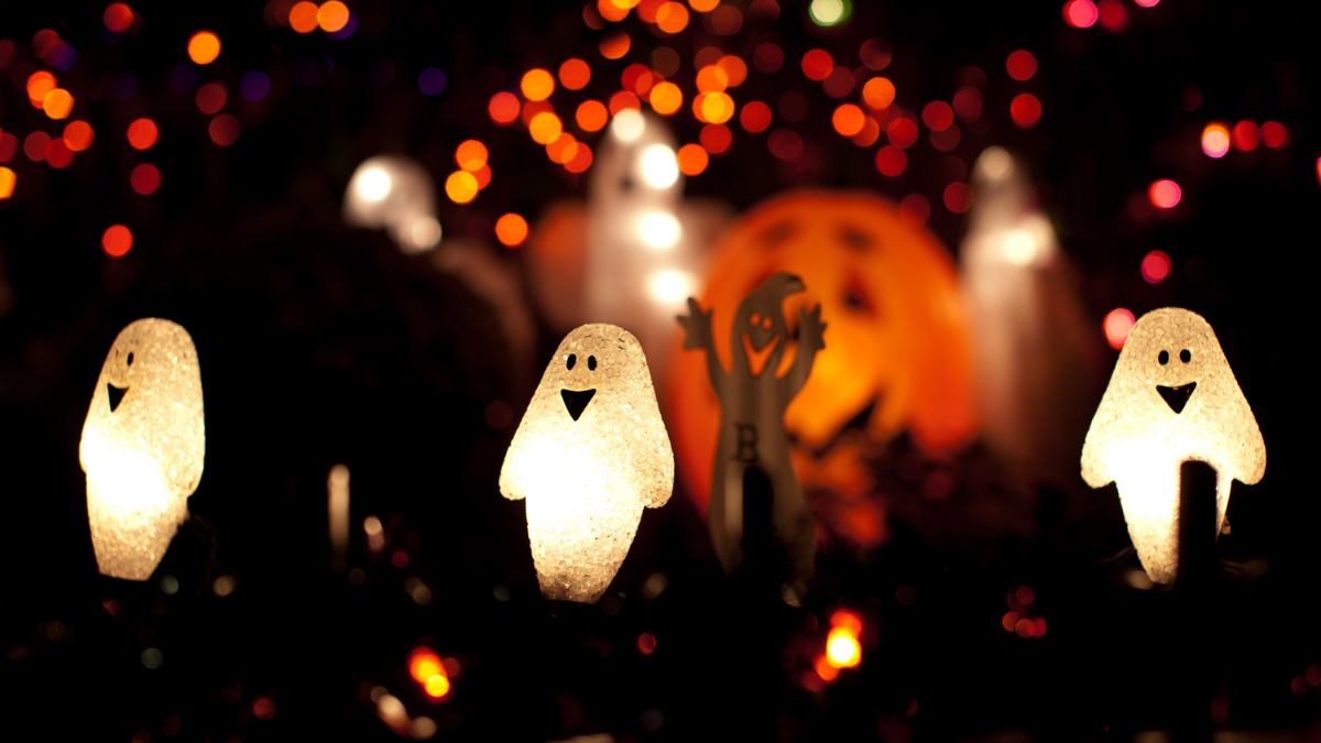 Glowing Halloween ghost decorations with pumpkin lantern and colorful lights in the background, creating a spooky festive vibe.